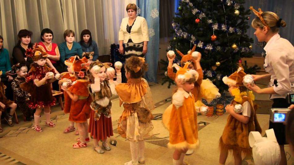 Девочки в костюмах белочек танцуют на новогоднем утреннике в детском саду.